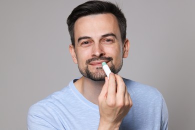 Photo of Handsome man applying lip balm onto his lips on grey background