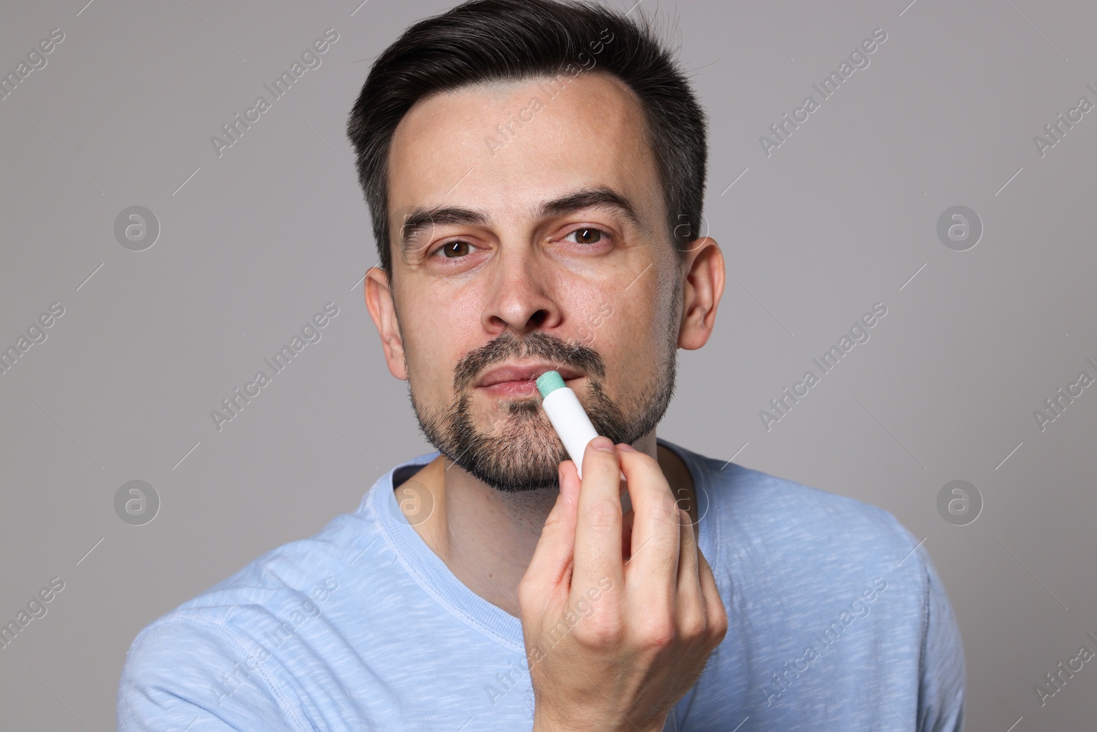 Handsome man applying lip balm onto his lips on grey background Photo of Handsome man applying lip balm onto his lips on grey background