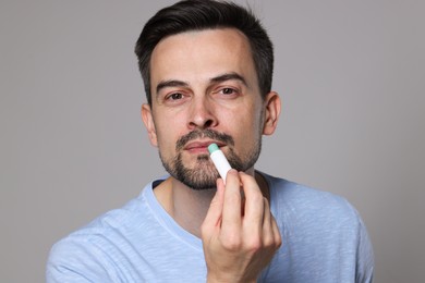 Photo of Handsome man applying lip balm onto his lips on grey background