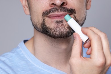 Photo of Man applying lip balm onto his lips on grey background, closeup