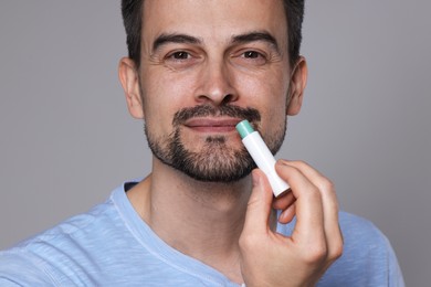 Photo of Handsome man applying lip balm onto his lips on grey background