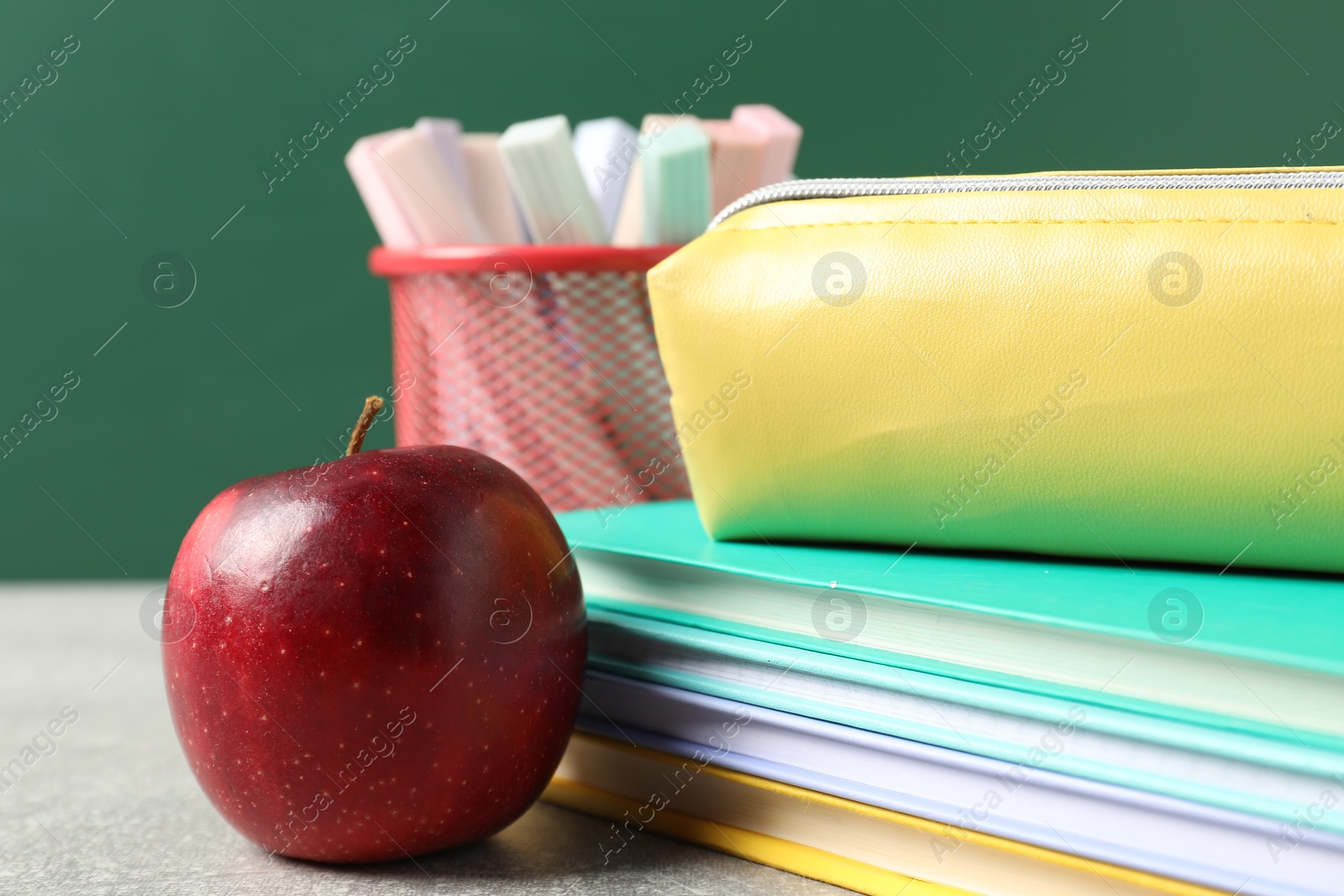 Different school stationery and red apple on grey table against blackboard, closeup Photo of Different school stationery and red apple on grey table against blackboard, closeup