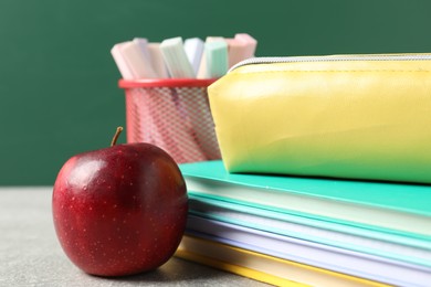 Photo of Different school stationery and red apple on grey table against blackboard, closeup
