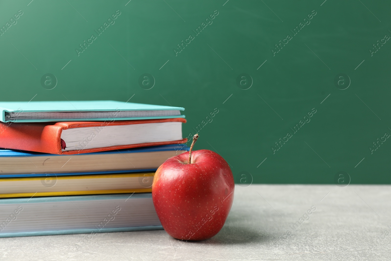 Different books and red apple on grey table against blackboard, closeup. Space for text Photo of Different books and red apple on grey table against blackboard, closeup. Space for text