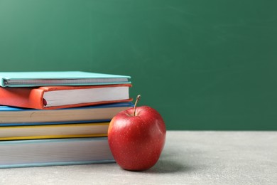 Photo of Different books and red apple on grey table against blackboard, closeup. Space for text