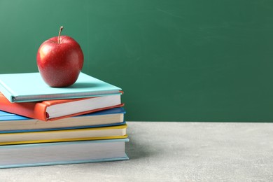 Photo of Different books and red apple on grey table against blackboard, closeup. Space for text