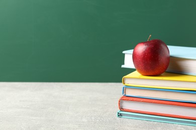 Photo of Different books and red apple on grey table against blackboard, closeup. Space for text