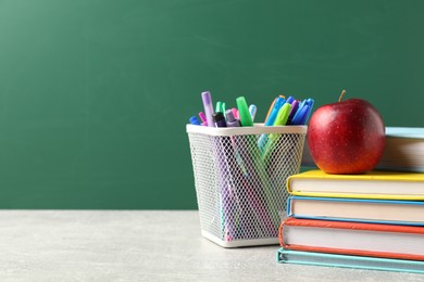 Photo of Different school stationery and red apple on grey table against blackboard, space for text