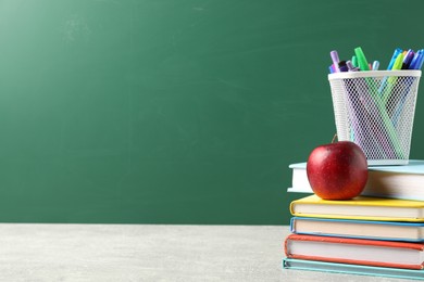 Photo of Different school stationery and red apple on grey table against blackboard, space for text