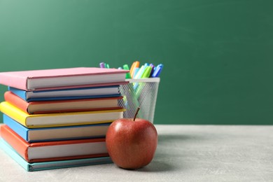 Photo of Different school stationery and red apple on grey table against blackboard, space for text