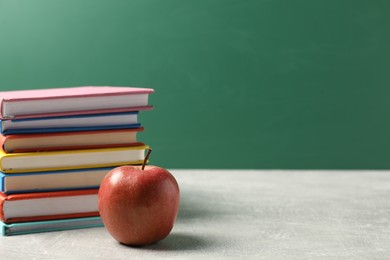 Photo of Different books and red apple on grey table against blackboard, space for text