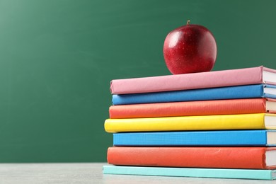 Photo of Different books and red apple on grey table against blackboard, low angle view. Space for text