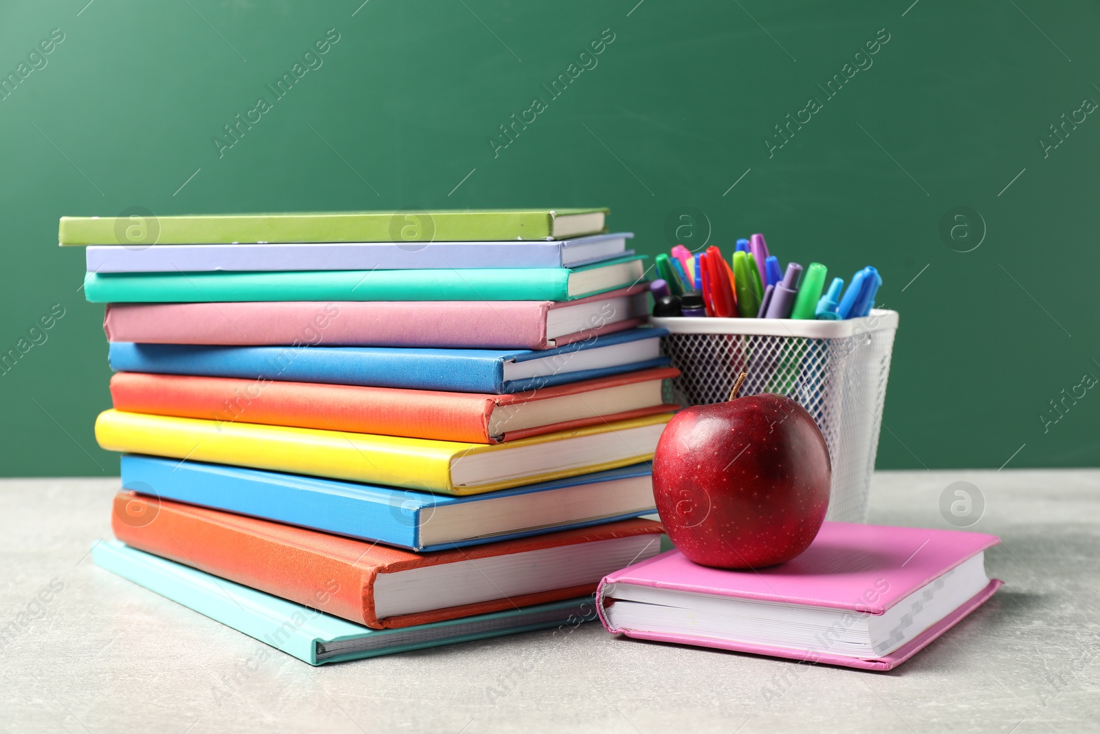 Different school stationery and red apple on grey table against blackboard Photo of Different school stationery and red apple on grey table against blackboard