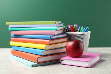Photo of Different school stationery and red apple on grey table against blackboard