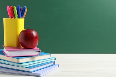 Photo of Different school stationery and red apple on white wooden table against blackboard, space for text