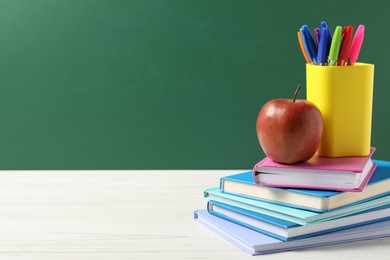 Photo of Different school stationery and red apple on white wooden table against blackboard, space for text