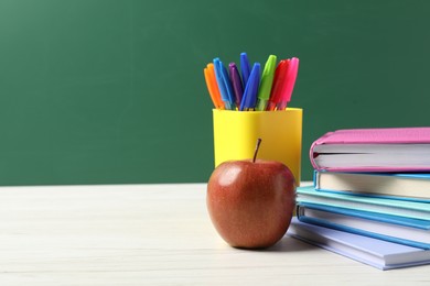 Photo of Different school stationery and red apple on white wooden table against blackboard, space for text
