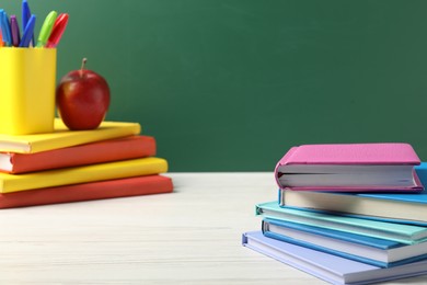 Photo of Different school stationery and red apple on white wooden table against blackboard, closeup