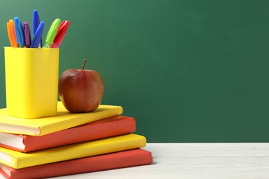 Photo of Different school stationery and red apple on white wooden table against blackboard, space for text