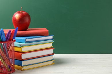 Photo of Different school stationery and red apple on white wooden table against blackboard, space for text