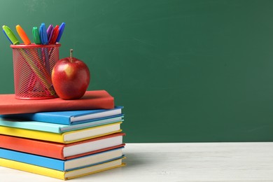 Photo of Different school stationery and red apple on white wooden table against blackboard, space for text