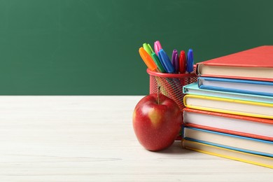 Photo of Different school stationery and red apple on white wooden table against blackboard, space for text