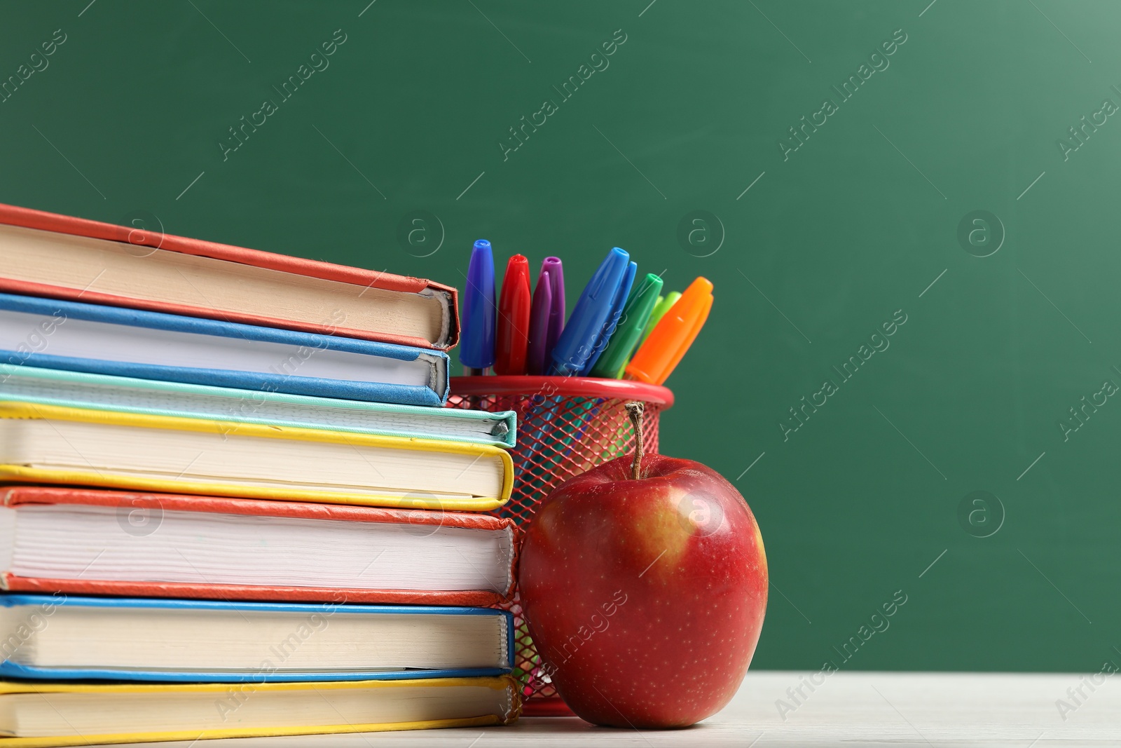 Different school stationery and red apple on white wooden table against blackboard, closeup. Space for text Photo of Different school stationery and red apple on white wooden table against blackboard, closeup. Space for text