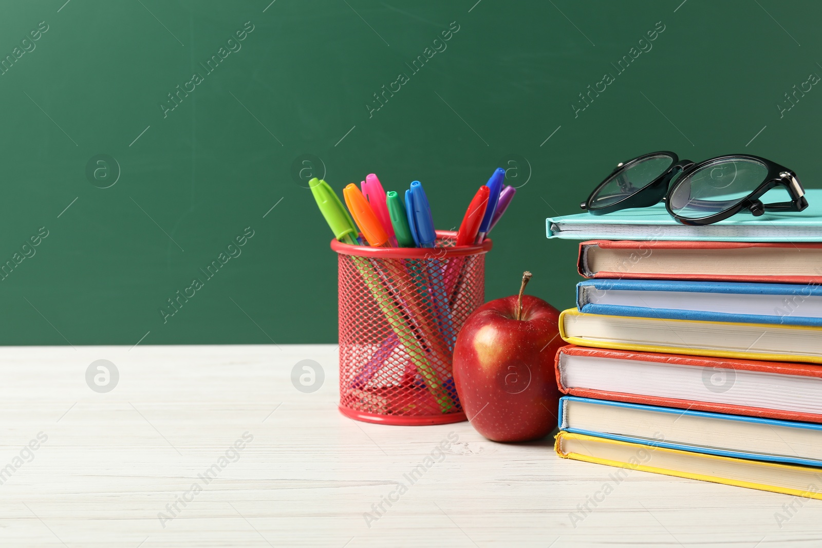Different school stationery, glasses and red apple on white wooden table against blackboard, space for text Photo of Different school stationery, glasses and red apple on white wooden table against blackboard, space for text