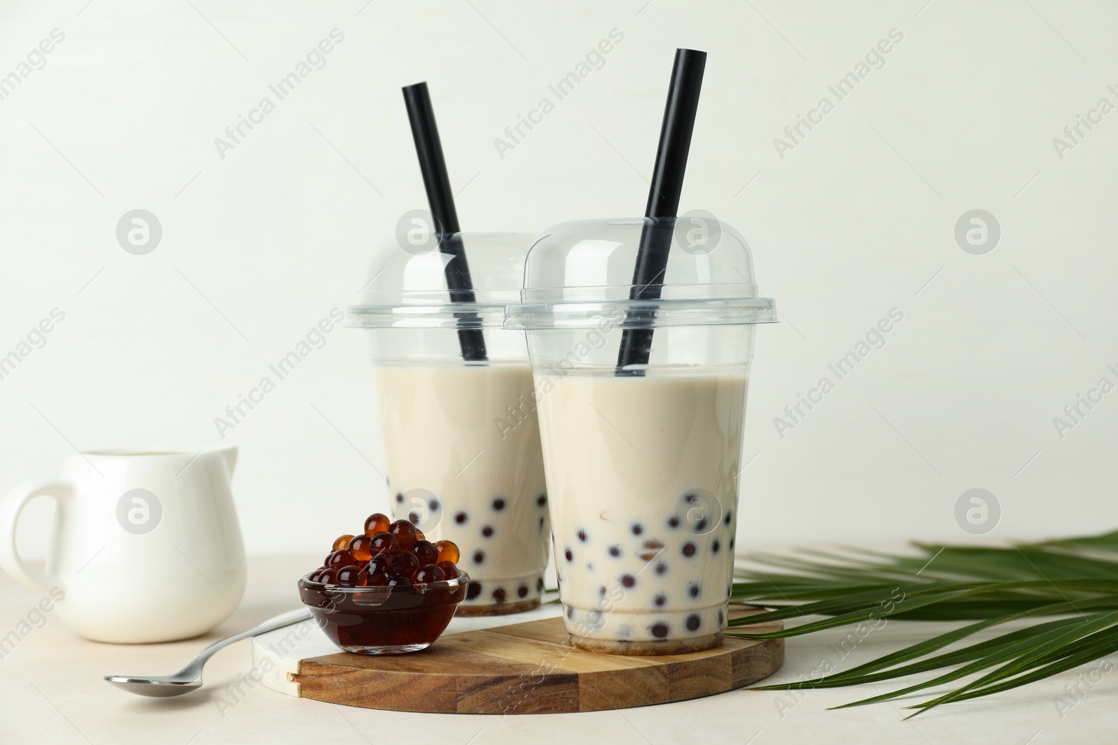 Tasty milk bubble tea in plastic cups, tapioca pearls and green leaves on beige table Photo of Tasty milk bubble tea in plastic cups, tapioca pearls and green leaves on beige table