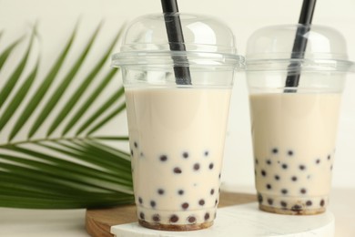 Photo of Tasty milk bubble tea in plastic cups and green leaves on beige table, closeup