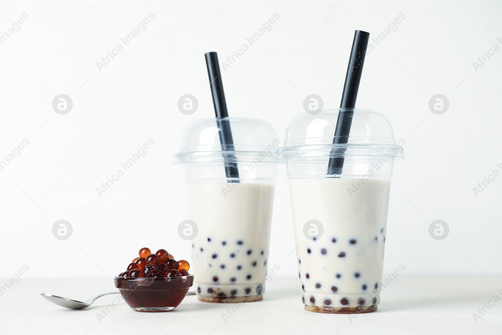 Tasty milk bubble tea in plastic cups and tapioca pearls on white table Photo of Tasty milk bubble tea in plastic cups and tapioca pearls on white table