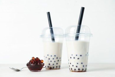Photo of Tasty milk bubble tea in plastic cups and tapioca pearls on white table