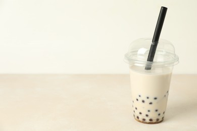 Photo of Tasty milk bubble tea in plastic cup on beige table, space for text