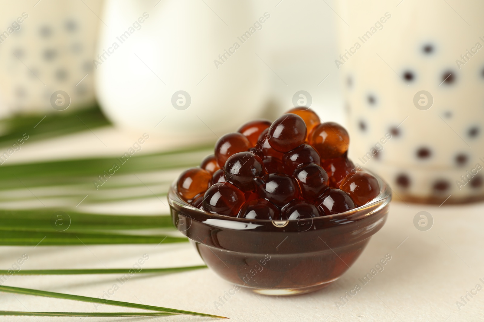 Tapioca pearls in bowl, bubble tea and green leaves on white table, closeup Photo of Tapioca pearls in bowl, bubble tea and green leaves on white table, closeup
