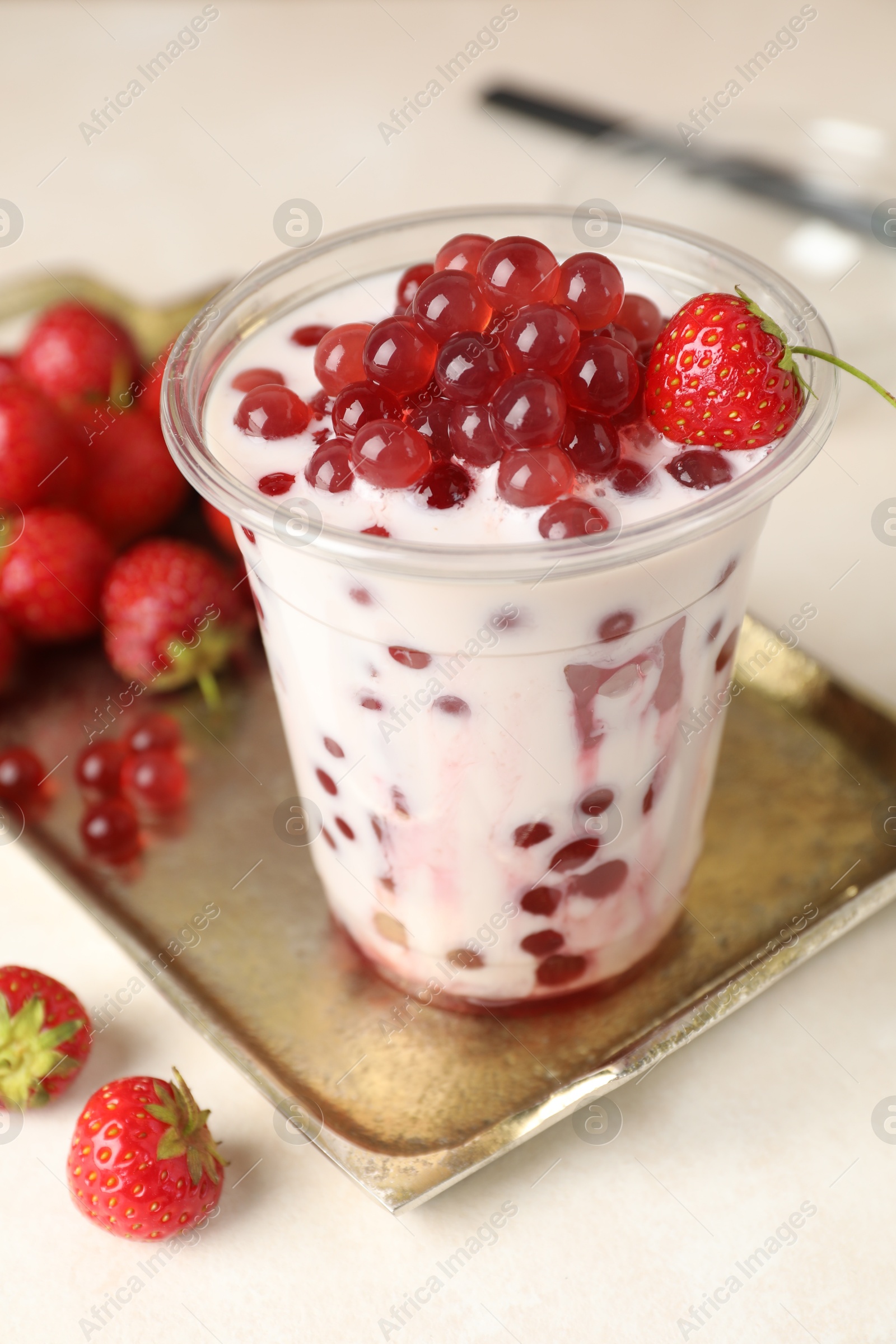 Tasty milk bubble tea in plastic cup and strawberries on white table, closeup Photo of Tasty milk bubble tea in plastic cup and strawberries on white table, closeup