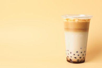 Photo of Tasty milk bubble tea in plastic cup on beige background, space for text