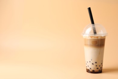 Photo of Tasty milk bubble tea in plastic cup on beige background, space for text