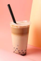 Photo of Tasty milk bubble tea in plastic cup on pink background, closeup