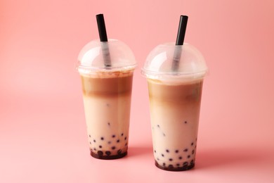 Photo of Tasty milk bubble tea in plastic cups on pink background