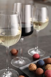 Photo of Tasty wine in glasses and truffle bonbons on grey table, closeup