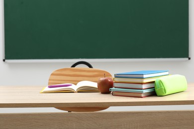 Photo of Different school stationery and apple on wooden table near blackboard indoors