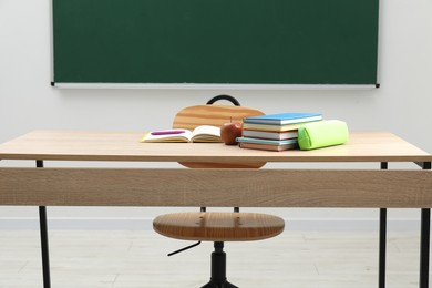 Photo of Different school stationery and apple on wooden table near blackboard indoors