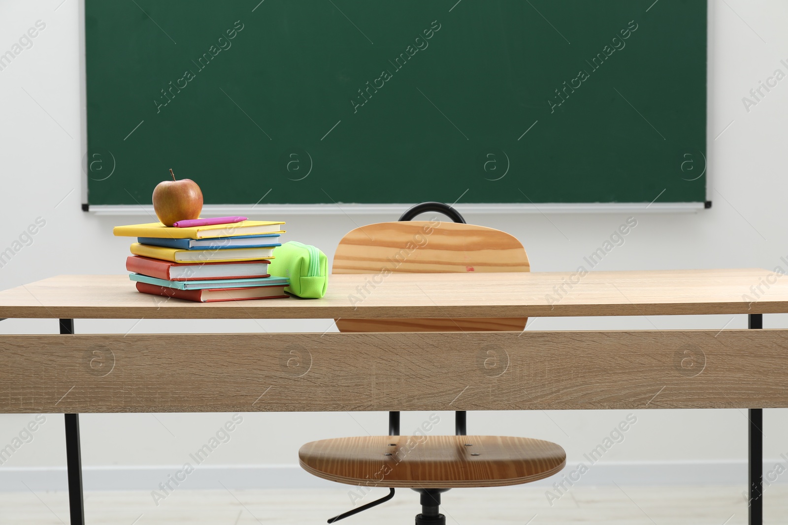 Different school stationery and apple on wooden table near blackboard indoors Photo of Different school stationery and apple on wooden table near blackboard indoors