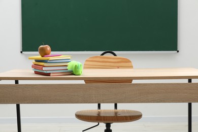 Photo of Different school stationery and apple on wooden table near blackboard indoors