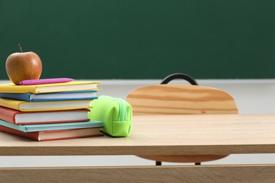 Photo of Different school stationery and red apple on wooden table near blackboard indoors, space for text