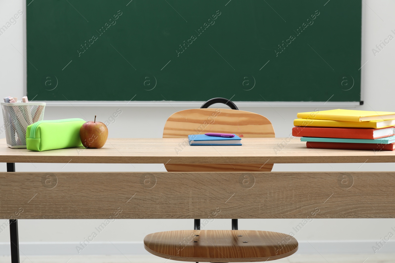 Different school stationery and apple on wooden table near blackboard indoors Photo of Different school stationery and apple on wooden table near blackboard indoors