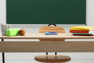 Photo of Different school stationery and apple on wooden table near blackboard indoors