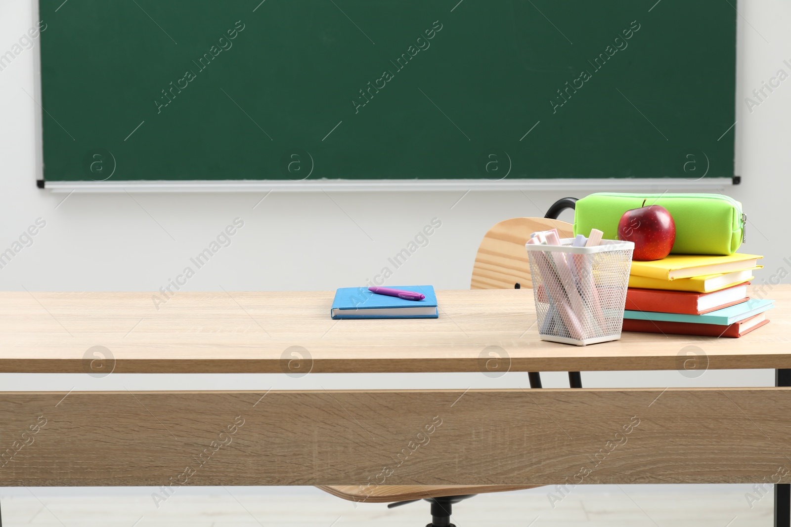 Different school stationery and red apple on wooden table near blackboard indoors Photo of Different school stationery and red apple on wooden table near blackboard indoors