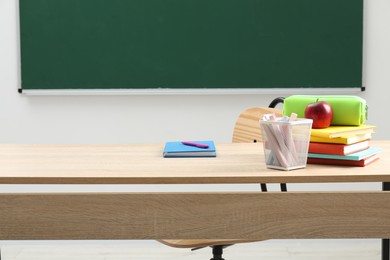 Photo of Different school stationery and red apple on wooden table near blackboard indoors