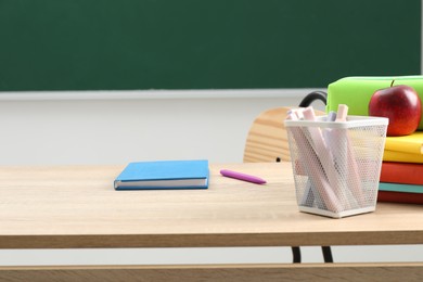 Photo of Different school stationery and red apple on wooden table near blackboard indoors
